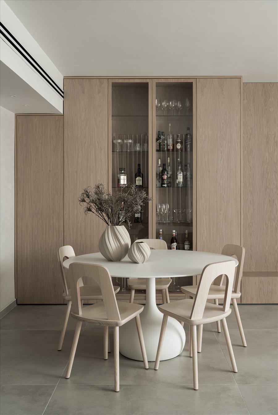 שולחן אוכל עגול בגוון בהיר, מוקף כיסאות עץ בקווים רכים